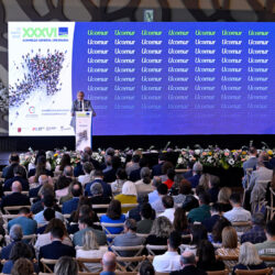 Foto con una persona delante de un atril y ante un aforo numeroso de personas asistentes a la asamblea de UCOMUR, union de Cooperativas de Murcia